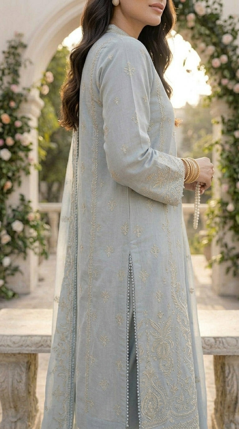 Woman in a light blue embroidered traditional outfit standing in a decorated outdoor setting.