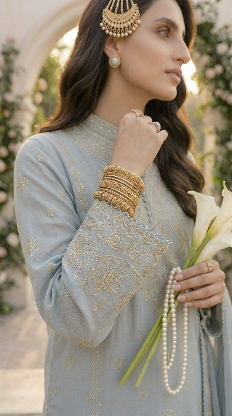 Woman in light blue traditional outfit with gold embroidery, holding a bouquet of white flowers.