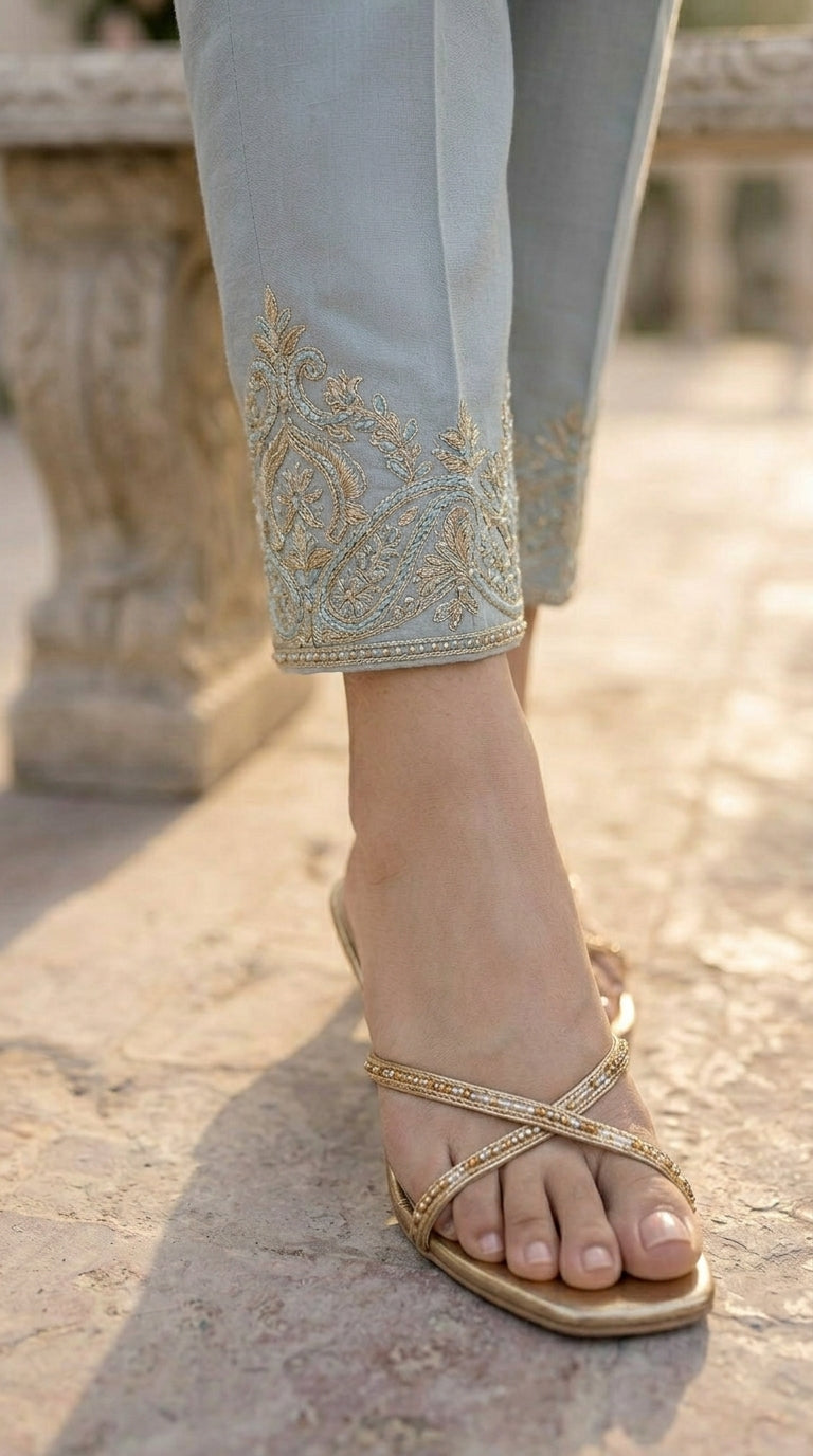 Close-up of a foot wearing a gold sandal on a stone surface.