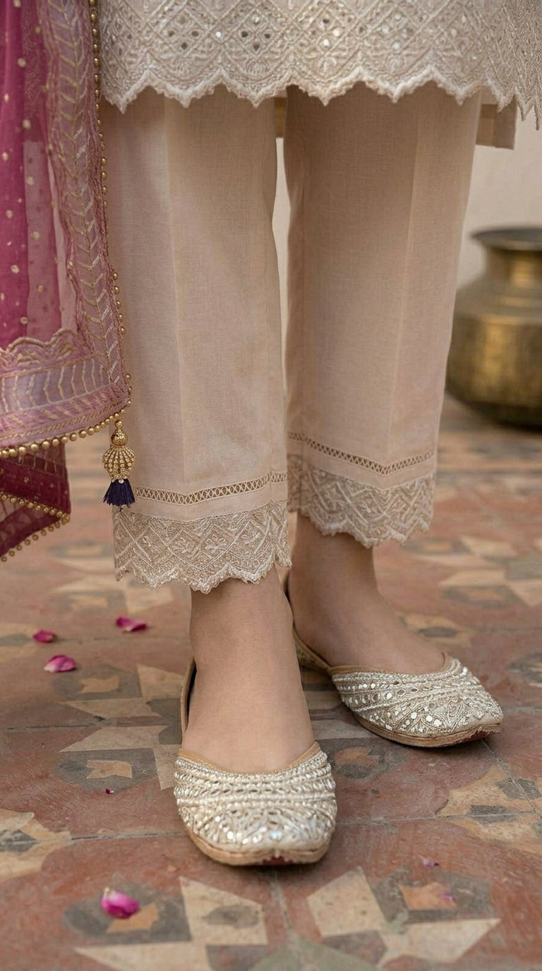 Beige traditional outfit with lace details and gold shoes on a patterned floor.