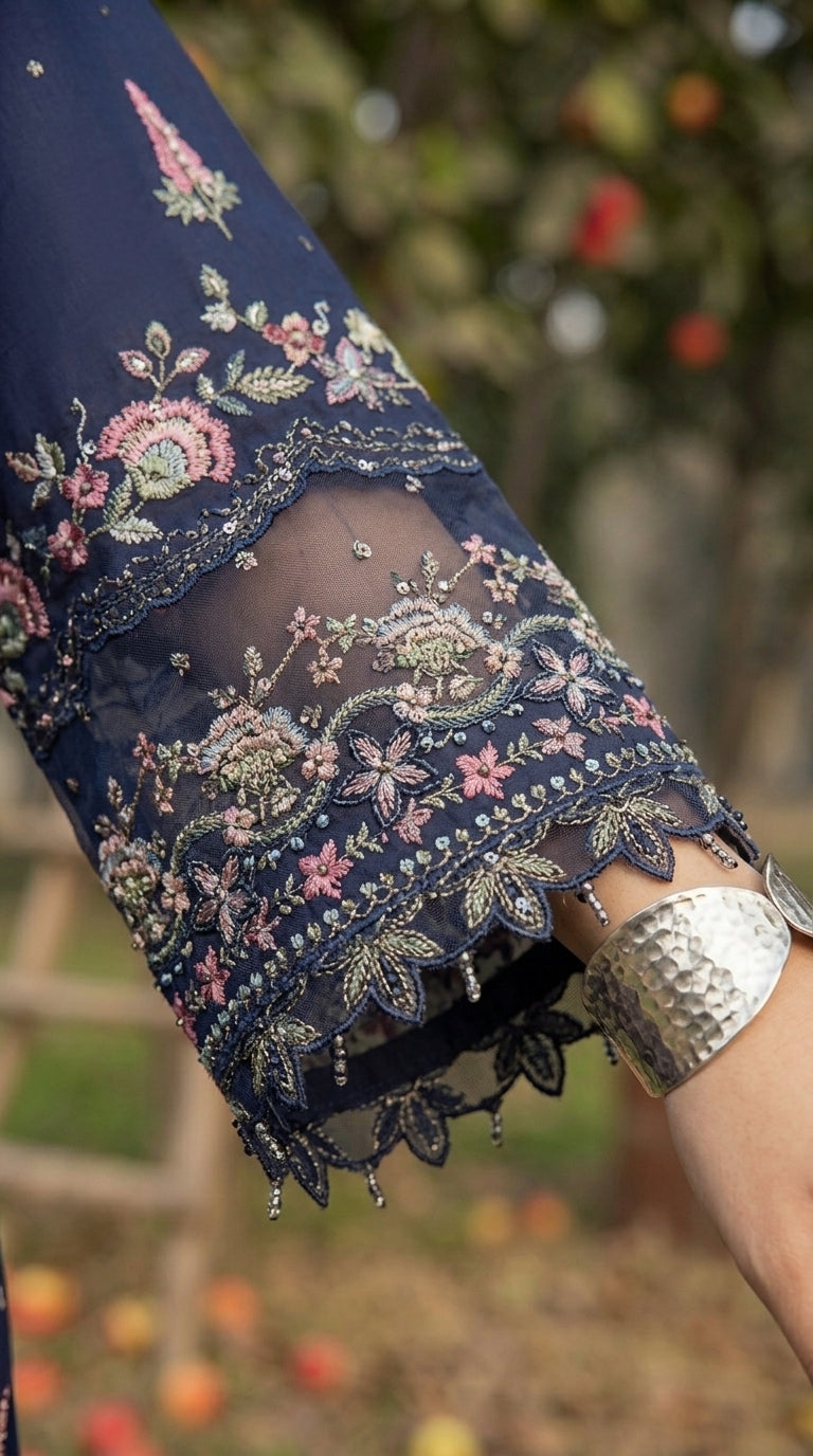 Close-up of a navy blue embroidered sleeve with floral patterns, held by a person wearing a silver bracelet.