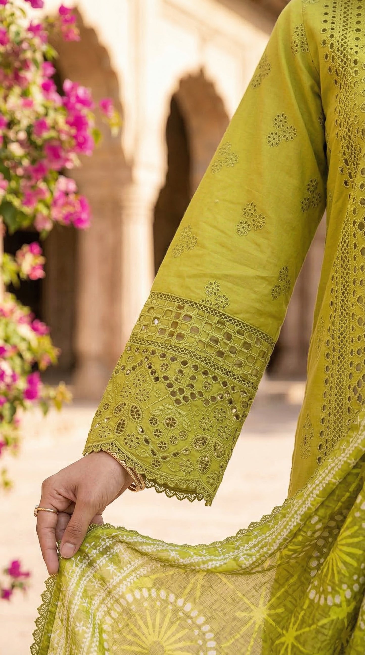 Close-up of a green embroidered garment with a blurred floral and architectural background